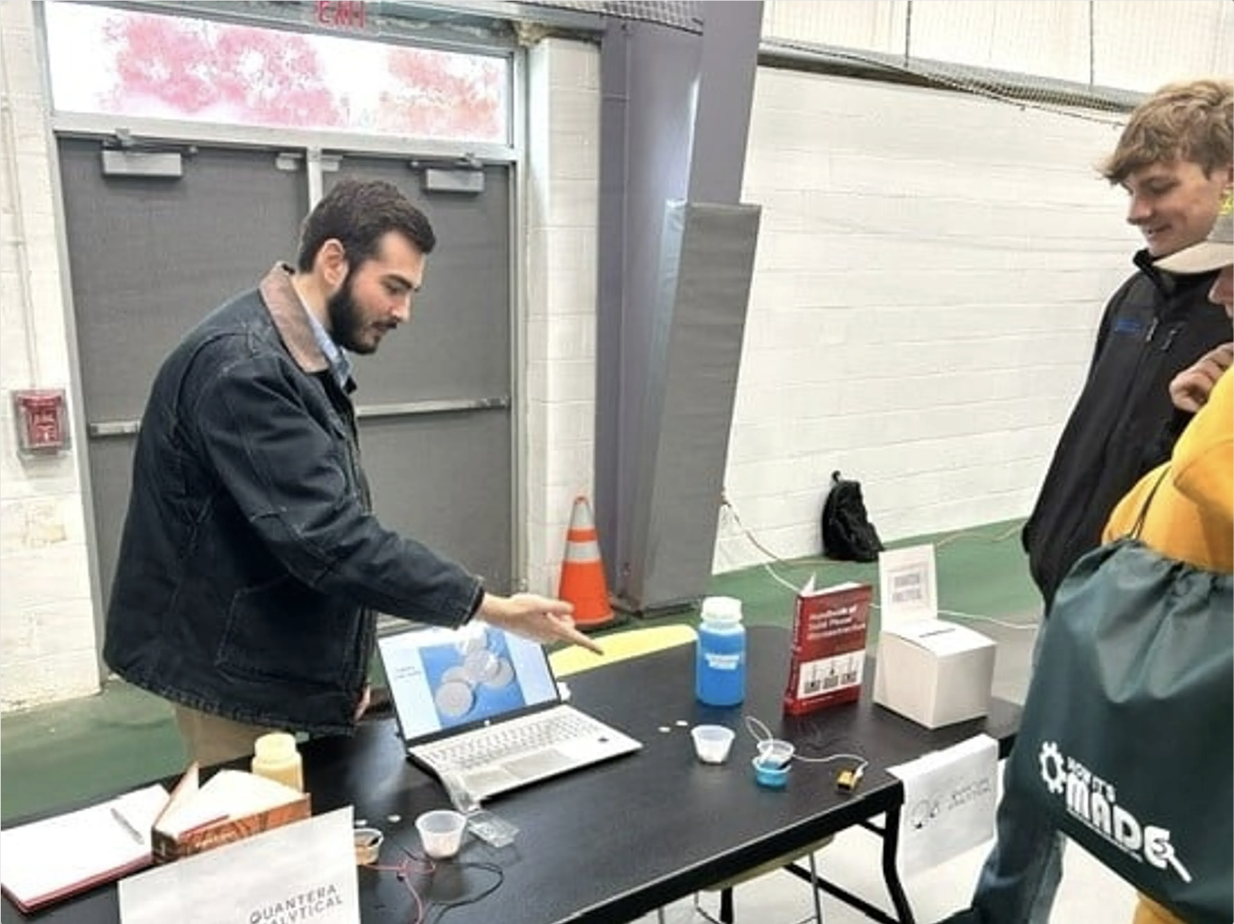 A man demonstrating a science experiment involving liquids at a table while three other people observe at an indoor event.