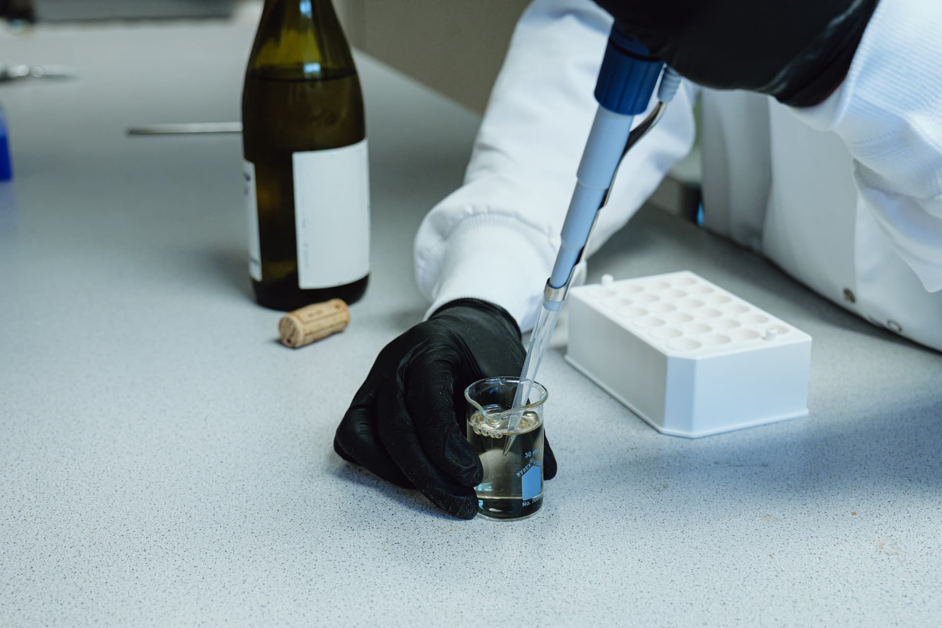 A gloved hand drawing a sample into a pipette beside a white multiwell sample plate